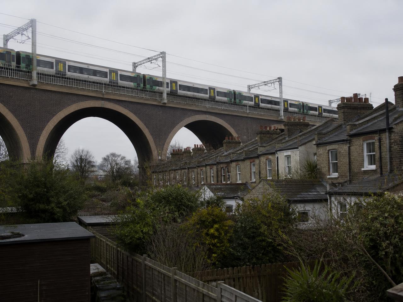 Electric commuter train crossing a brick viaduct directly behind the rear gardens of terraced houses